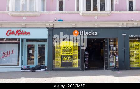 Obdachloser Mann, der in der Tür des geschlossenen Cath Kidston Shops schläft Neben dem Blacks Outdoor Shop, der einen Vorrat hat Sonderangebote in North Street Brighton Stockfoto