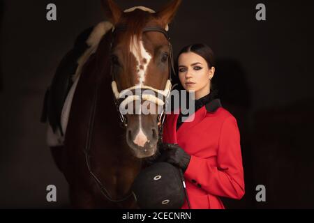 Reiter Jockey Frau Umarmungen mit braunem Pferd, schwarzer Hintergrund Stockfoto