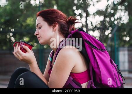 Junge Sportlerin, die auf der Bank sitzt und Kaffee trinkt Stockfoto