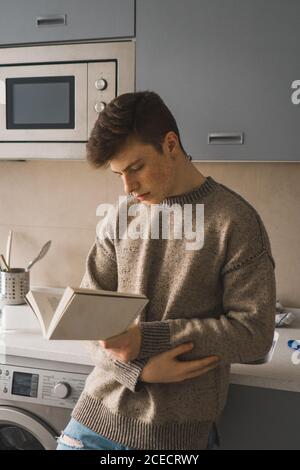 Zwangloser Mann liest Buch in der Küche Stockfoto