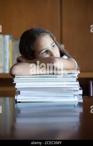 Gelangweiltes Mädchen, das sich auf einen Stapel Bücher stützt, die hineinstarren Unendlich Stockfoto