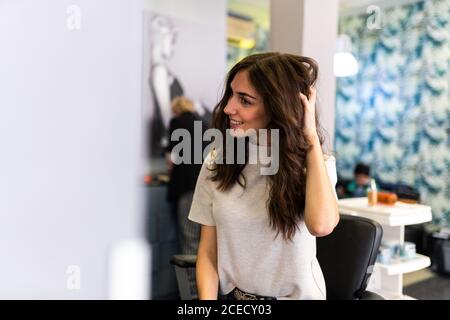 Reflexion der jungen schönen Frau berühren Haar an Spiegel im Friseursalon suchen Stockfoto