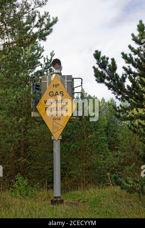 Ein substantieller Metallmarker mit einem gelben Warnschild, das den Punkt markiert, an dem eine Gasleitung die Tay-Mündung im Tentsmuir-Wald überquert. Stockfoto