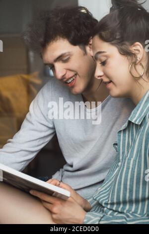 Glücklicher junger Mann und Frau sitzen zusammen und lesen zu Hause ein Buch. Stockfoto