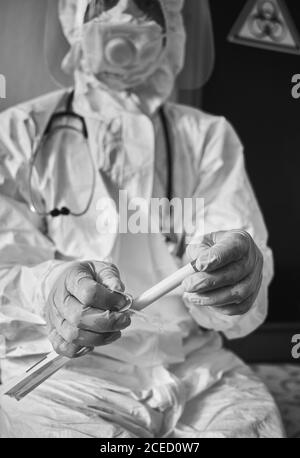 Vertikaler Ausschnitt eines Arztes mit COVID-19-Abstrichbesteck, weißem Schutzanzug, Atemschutzmaske, Handschuhen, Reagenzglas zur Entnahme von OP NP-Patientenproben, Biogefahrenschild auf dem Hintergrund Stockfoto
