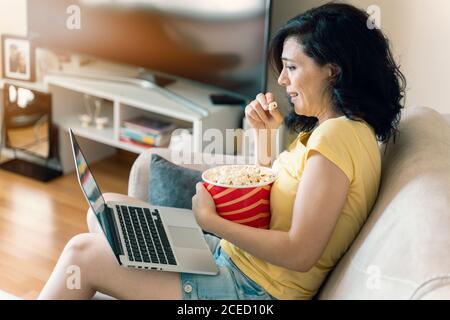 Verängstigte junge Frau, die zu Hause einen gruseligen Film sieht. Mädchen beobachten einen Terror Horrorfilm auf Laptop sitzen auf einer Couch zu Hause. Scary Movie Night Stockfoto