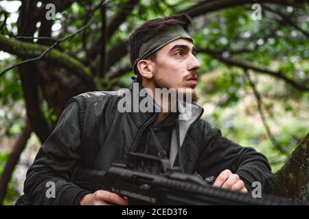 Soldat oder revolutionäres Mitglied oder Jäger in Tarnung auf dem Baum, der die Waffe in der Hand beobachtet Stockfoto