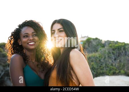 Schöne, vielfältige junge Frauen, die nahe stehen und glücklich lächeln Hintergrund der Natur im Hintergrund beleuchtet Stockfoto