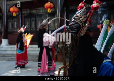 GUINZHOU, CHINA - 14. JUNI 2018: Gruppe der ethnischen Minderheit Miao Frauen in hellen traditionellen Kostümen und Masken stehen mit Mann in gelben Kostümen im Freien an der Wand des chinesischen Gebäudes in Guizhou Stockfoto