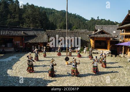 GUINZHOU, CHINA - 14. JUNI 2018: Frauen der Miao Ethnie in hellen Kostümen mit bunten Ornamenten und Kopfschmuck Durchführung traditionellen Festtanz auf Dorfplatz an sonnigen Sommertag in der Provinz Guizhou in China Stockfoto