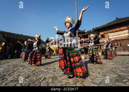 GUINZHOU, CHINA - 14. JUNI 2018: Frauen der Miao Ethnie in hellen Kostümen mit bunten Ornamenten und Kopfschmuck Durchführung traditionellen Festtanz auf Dorfplatz an sonnigen Sommertag in der Provinz Guizhou in China Stockfoto