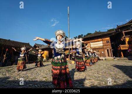 GUINZHOU, CHINA - 14. JUNI 2018: Frauen der Miao Ethnie in hellen Kostümen mit bunten Ornamenten und Kopfschmuck Durchführung traditionellen Festtanz auf Dorfplatz an sonnigen Sommertag in der Provinz Guizhou in China Stockfoto