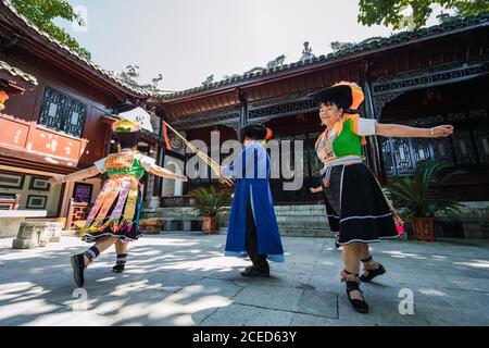 GUINZHOU, CHINA - 14. JUNI 2018: Miao Ethnie Mann in blauen Kleidern spielen traditionelle Musikinstrumente und Frauen in hellen lokalen Kostümen tanzen um ihn herum während des Festivals im Dorf in der Provinz Guizhou in China Stockfoto