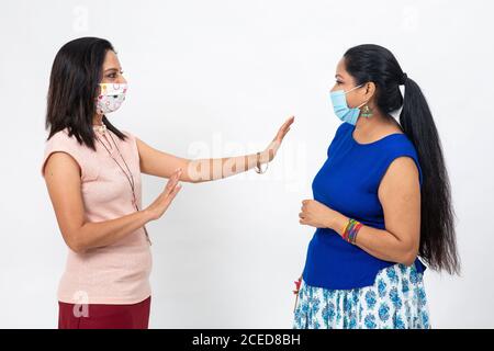 Zwei hübsche indische Frauen tragen Covid-19 Schutzmaske. Zwei Weibchen weisen auf eine soziale Distanzierung zwischen sich hin. Stockfoto