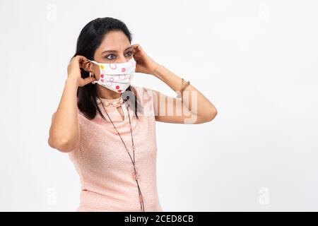 Hübsche indische Frau trägt Covid-19 Schutzmaske. Frau mit professionellem Look steht vor weißem Hintergrund Stockfoto
