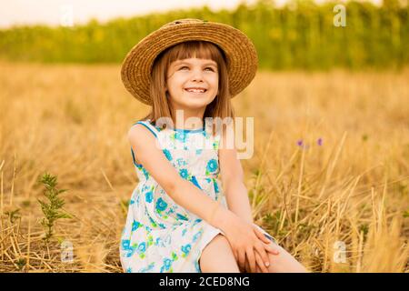 Hübsches kleines Mädchen in Strohhut und Kleid Spaziergang im Sommer Feld. Sonniger Tag, stilvolles Kind Stockfoto