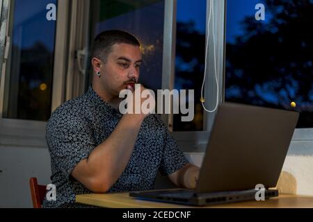 Nahaufnahme eines jungen Mannes, der an einem Laptop arbeitet Sitzen neben offenen Fenstern in den Abendstunden Stockfoto