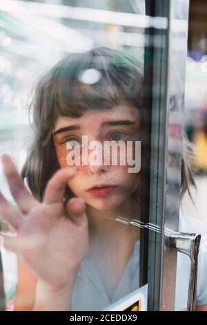 Kindisch junge Frau mit entzückenden Sommersprossen Gesicht berühren Fenster Glas Stockfoto