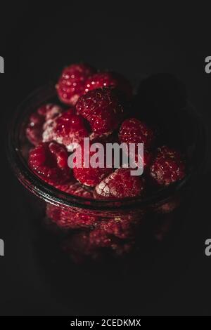 Nahaufnahme von leckeren reifen Himbeeren liegen im Glas Im dunklen Zimmer Stockfoto