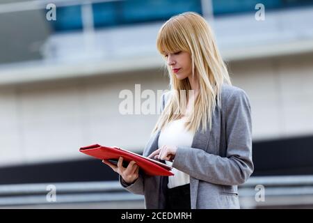 Schöne blonde Frau im Anzug auf der Straße stehen und mit Tablet Stockfoto