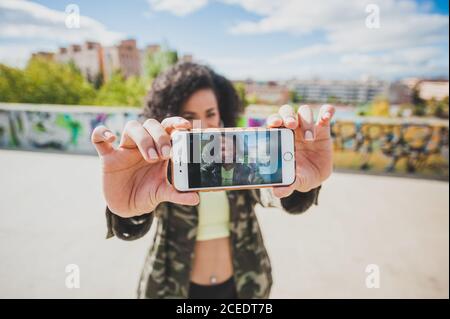 Nahaufnahme des Bildschirms des Smartphones mit lächelnder junger Frau, die im Freien Selfie im Sonnenlicht nimmt Stockfoto