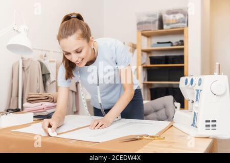 Junge Schneiderin Frau näht Kleidung auf Nähmaschine in Designer-Studio. Kreidemuster auf Stoff Stockfoto