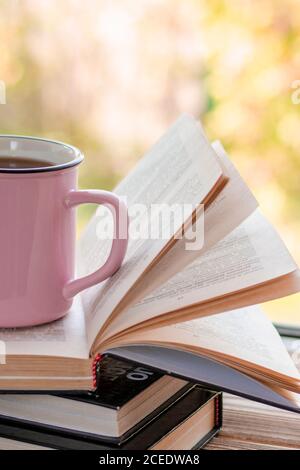 Eine rosa Tasse Tee steht auf einem Stapel von Öffnen Sie Bücher Stockfoto