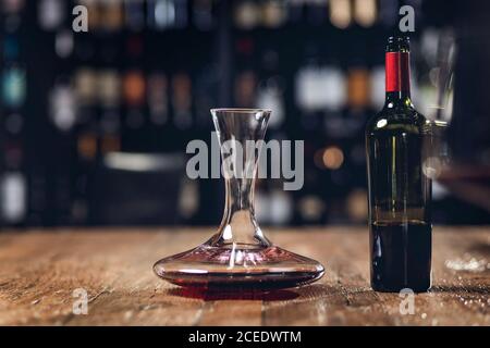 Rotwein in Flasche und Dekanter steht auf Holztisch im Restaurant, dunkler Hintergrund Stockfoto