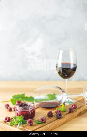 Frische hausgemachte Himbeermarmelade mit Wein und Minze im Glas auf einem hölzernen Hintergrund. Mehrere frische Beeren, Glas und eine Flasche Wein sind in der Nähe. Stockfoto