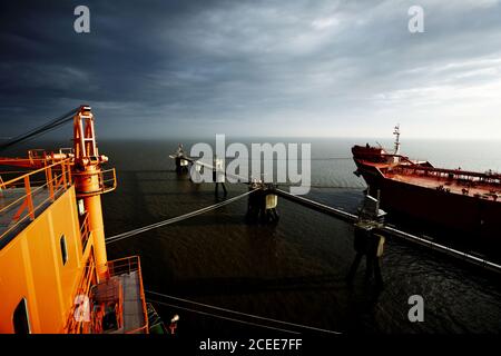 Ein großer Öltanker am Dock. Großes Gebäude auf der linken Seite und ruhiges Wetter. Dunkler, wolkig Himmel und schwarzes Wasser. Stockfoto