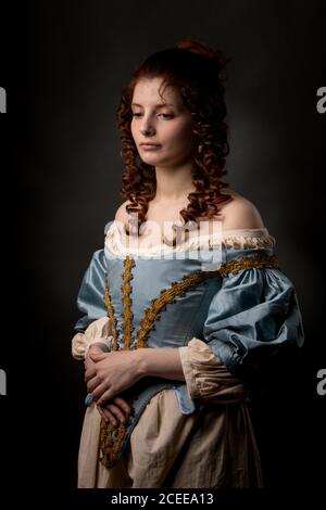 Attraktive junge Dame in wunderschönen barocken Kleid halten die Hände auf Bauch beim Stehen auf schwarzem Hintergrund Stockfoto