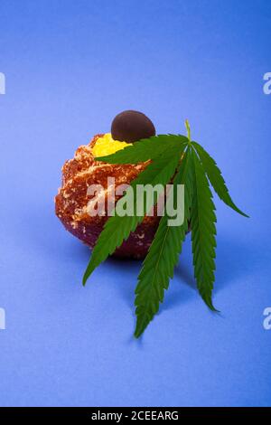 Frischer süßer Cupcake mit Marihuana-Pflanzenblatt auf blauem Hintergrund, Süßigkeiten mit Cannabis, süßes Gebäck, Dessert. Stockfoto