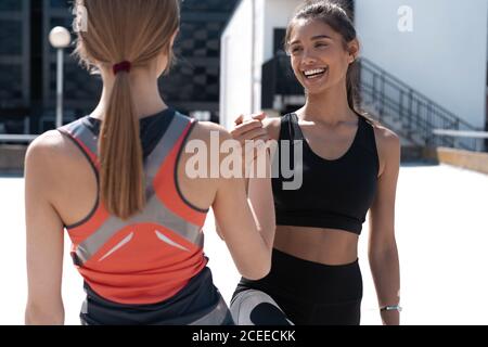 Zwei fröhliche Frauen in Fitness tragen geben hohe fünf während Laufen in der Stadt Stockfoto