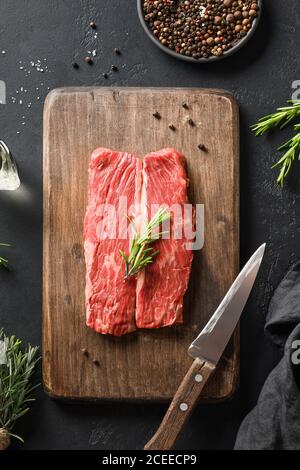 Rohes marmoriertes Ribeye Steak mit Rosmarinzweig auf Schneidebrett. Vertikale Zusammensetzung. Stockfoto