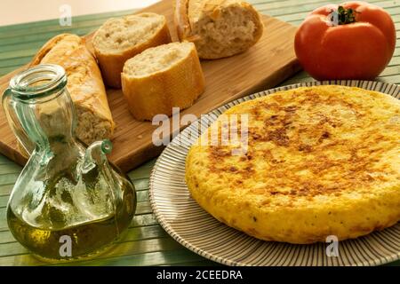 Spanische Tortilla auf einem rustikalen Teller mit einem Glas Von Olivenöl und etwas Brot auf und ein hölzernes Tischdecke Stockfoto