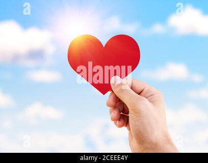 Mann Hand hält rotes Papier Herz gegen schönen blauen Himmel. Konzept der Liebe, Gefühle und Emotionen. Stockfoto