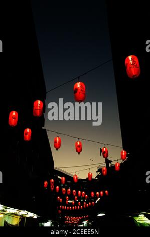 Von unten Aufnahme von roten chinesischen Laternen hängen an Seilen zwischen Gebäuden in der Dämmerung. Stockfoto