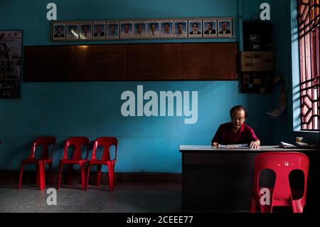 Reifer Mann sitzt am Tisch in der Halle neben dem Fenster mit Stühlen an der Wand im Hintergrund. Stockfoto