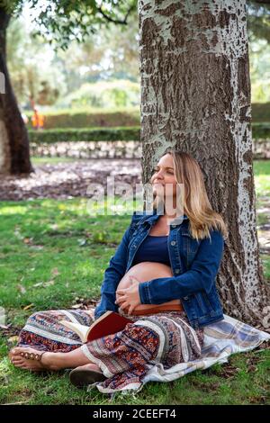 Lächelnd schwanger Attraktive Frau unter Baum sitzend Stockfoto