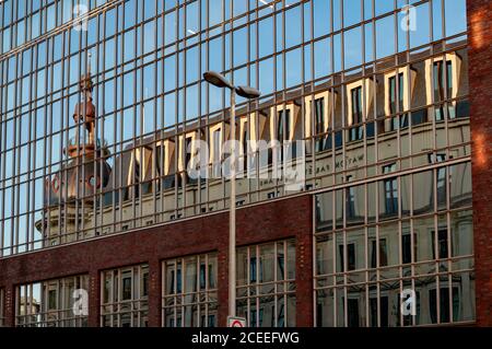 Goldenes Sonnenlicht in verzerrter Reflexion des historischen Gebäudes mit Kapellenturm in Glaswand reflektierende Oberfläche des modernen Gebäudes. Modern und c Stockfoto
