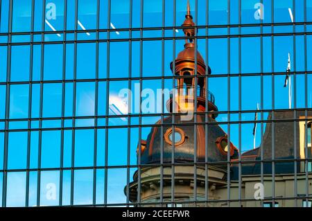 Verschwommenes Spiegelbild der Kapelle und des Glockenturms in der Spiegelwand des Wolkenkratzers. Verzerrte Spiegelung der Kathedrale und blauer Himmel in Glas Panoramafenstern o Stockfoto