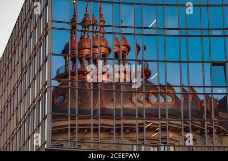 Spiegelung der Kapelle Dach in verspiegelter Wand. Verzerrte Reflexion in Glasfenstern. Firmengebäude außen mit blauen Glas-Panoramafenstern Stockfoto