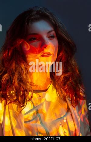 Nachdenkliche, tagträumende Frau, die in warmem Licht steht und im Studio wegschaut Stockfoto