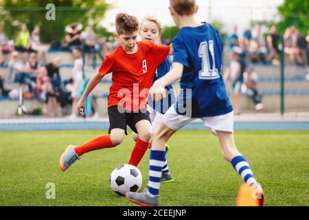 Jungen spielen Fußballspiel. Junior Wettbewerb zwischen Spielern laufen und treten Fußball. Ball. Jugendsportler in roten und blauen Fußballtrikots. Kinder Stockfoto