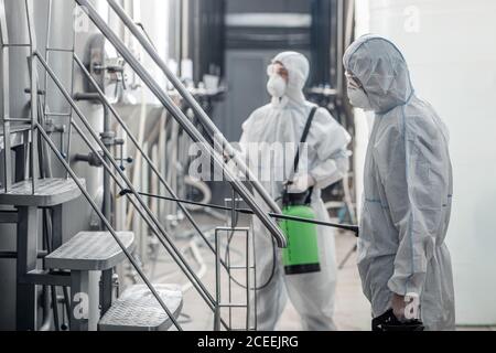 Reinigung und Desinfektion bei der Arbeit. Jungs in Schutzanzügen und Brille, arbeiten im Betrieb Stockfoto