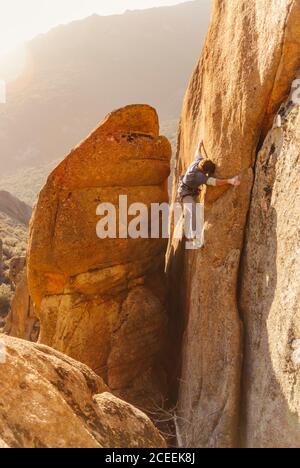 Sportiver Mann, der in den Abendlichtern auf einen Felsen klettert. Stockfoto