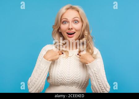 Stauned schockiert Frau mit lockigen blonden Haaren zeigt Finger auf sich selbst mit überraschenden Blick, kann nicht an ihren Sieg glauben, Erfolg. Innenaufnahme des Studios i Stockfoto