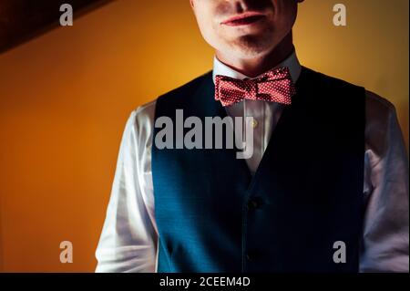 Crop junger Mann in Weste mit roter Fliege auf Hintergrund der gelben Wand. Stockfoto