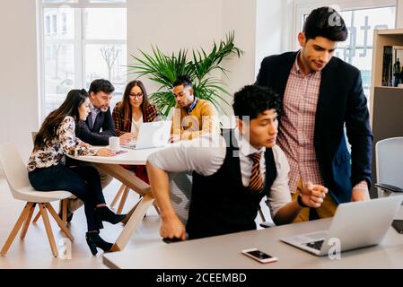 Männer und Frauen aus verschiedenen Rassen sitzen und stehen an Laptops, während sie gemeinsam arbeiten. Stockfoto