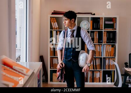 Schöner junger asiatischer Mann, der im Büro steht und wegschaut. Stockfoto